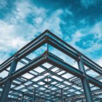 Steel frame structure of a modern building under construction showing metal beams against a cloudy blue sky