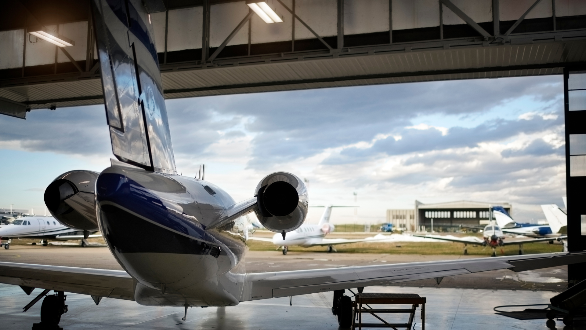 View from inside an aircraft hangar looking out toward multiple private jets parked on the tarmac under a cloudy sky, highlighting aviation operations and hangar functionality.
