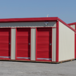 Exterior of a white self-storage facility with red unit doors, red roof, and ground-level drive-up access