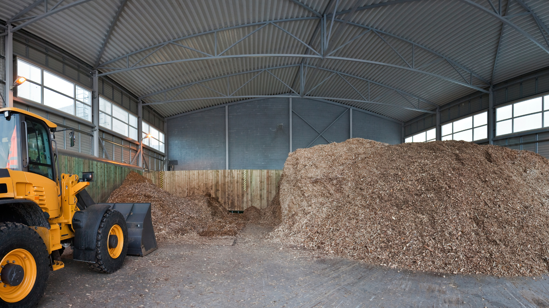 Farm equipment stored inside agricultural storage building with wood chip piles