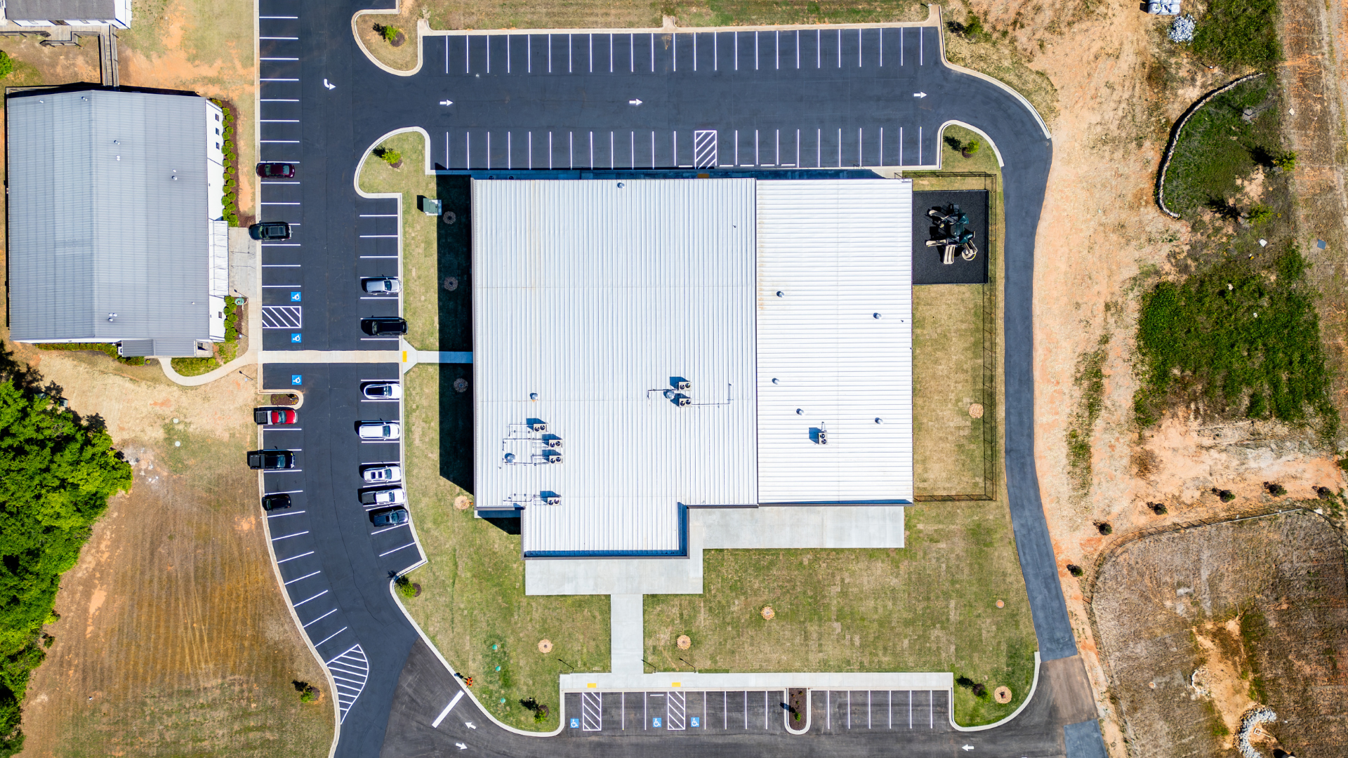Aerial top-down view of a completed metal building roof system with integrated parking layout and site planning, showcasing large-scale commercial roof design and drainage considerations.