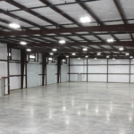 Interior of a clear-span steel building with insulated wall and roof panels, high-bay lighting, and an open floor plan. Proper maintenance and inspections help preserve structural performance, energy efficiency, and long-term durability.