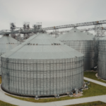 Large commercial grain storage silos connected by overhead conveyors at an agricultural grain handling facility.