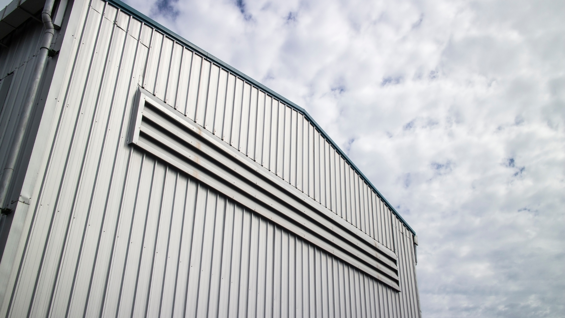 Exterior wall of a steel industrial building clad with vertical metal panels and ventilation louvers. Metal building envelopes provide durable protection, efficient installation, and long service life in commercial and industrial applications.