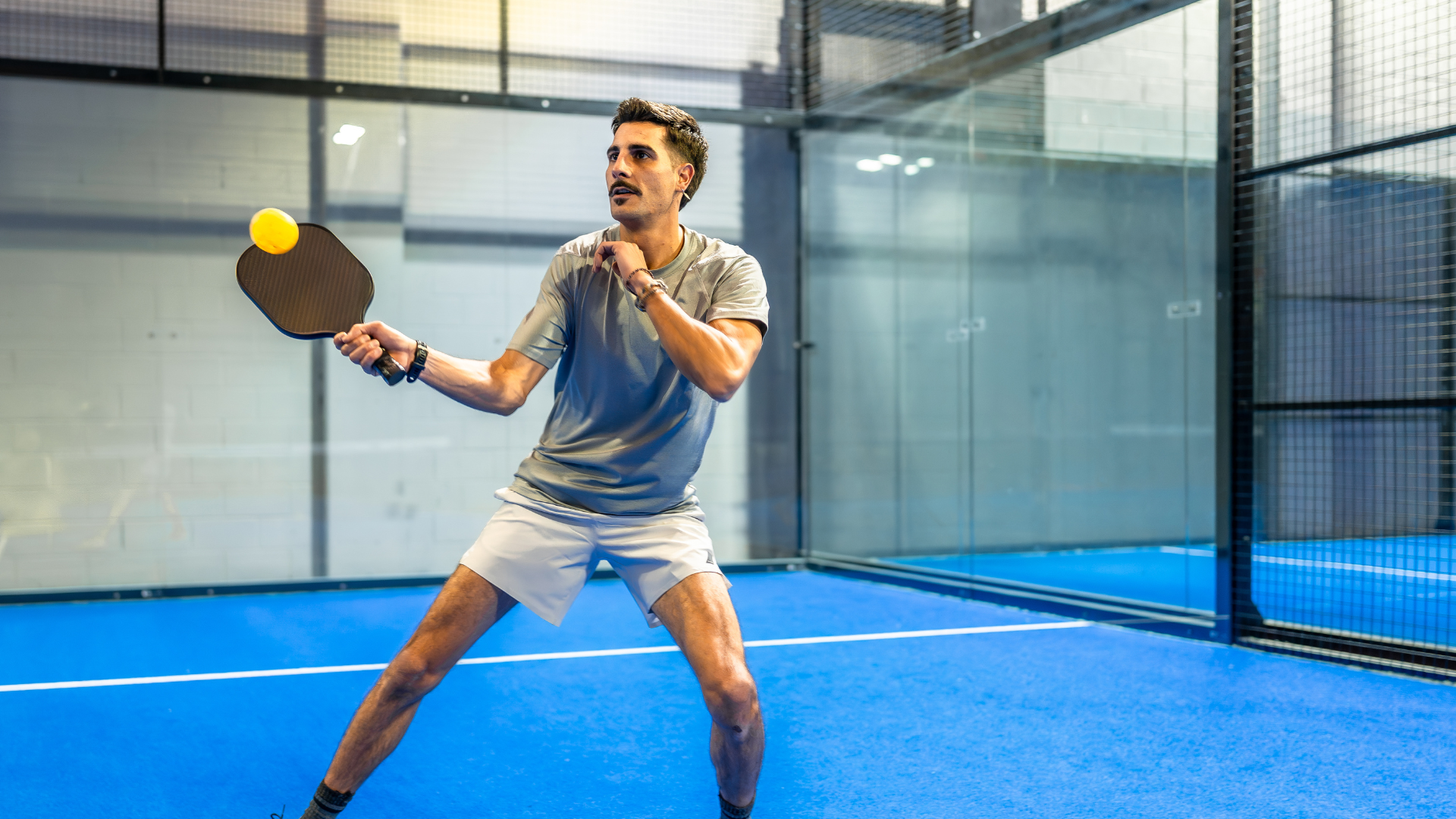 Player on an indoor pickleball court with proper lighting and court enclosure.