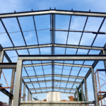 Steel frame structure under construction with exposed beams and columns against a blue sky.